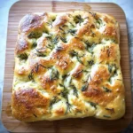 Golden-brown homemade rosemary focaccia bread with a crispy crust and soft interior, served on a wooden cutting board